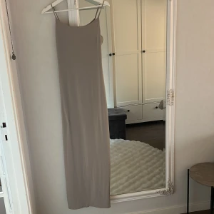 Beige långklänning från Bik Bok - Säljer en stilren beige långklänning från Bik Bok i storlek S. Klänningen har smala axelband och en rak, figurnära passform som ger en clean och modern look. Perfekt för dig som gillar minimalistisk stil och neutrala färger.