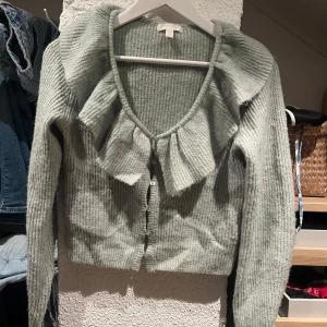 Ljusgrön stickad kofta med volang - Superfin ljusgrön stickad kofta från H&M med volangdetalj längs v-ringningen. Koftan är croppad och har långa ärmar samt knappar framtill. 