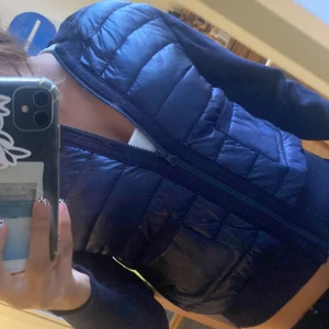 Mörkblå dunjacka från Gina Tricot - Snygg mörkblå dunjacka från Gina Tricot med quiltad framsida och två praktiska fickor. Västen har dragkedja hela vägen och ribbade muddar vid midjan och ärmslut. Perfekt för lager-på-lager och chill stil.