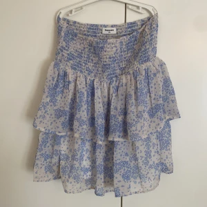 Blommig volangkjol från Kappahl - Supersöt kort volangkjol från Kappahl i vitt med blått blommönster. Kjolen har smock i midjan och dubbla lager för extra volym. Perfekt för dig som gillar en romantisk och somrig stil.