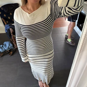 Vit och marinblå ribbad långklänning - Säljer en superfin långklänning med ribbad struktur i vit och marinblå. Klänningen har ett randigt mönster, lång ärm och sitter tight mot kroppen. Den har en bred, något båtformad halsringning och är gjord i ett stickat material som är både mjukt och följsamt. Sparsamt använd och perfekt om man vill vara extra fin men ändå bekväm! Den är vanlig i storleken