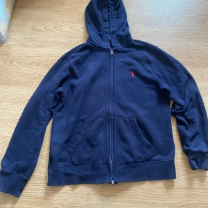 Mörkblå hoodie från Polo Ralph Lauren - Snygg mörkblå hoodie från Polo Ralph Lauren med röd logga. Den är gjord i mjuk bomull, perfekt för chill dagar. Långärmad och klassisk passform. Storleken vet ja ej helt för det står ej men skulle säga runt s den sitter som 152/156