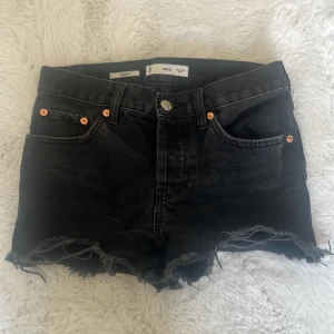 Svarta jeansshorts från MNG - Svarta jeansshorts från MNG och klassisk femficksdesign. Modellen är midwaist och har snygga kopparfärgade nitar vid fickorna. Perfekta för en chill sommarlook med lite edge.