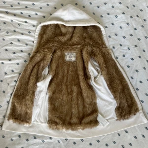 Vit vintage hoodiejacka med pälsfoder Abercrombie - Säljer en vintage vit hoodiejacka från Abercrombie & Fitch i storlek S. Jackan har mjukt brunt pälsfoder på insidan, huva och dragkedja framtill. Utsidan är slät och har två fickor. Perfekt för dig som gillar mysiga och stilrena plagg. Super trendig y2k viral på TikTok. 