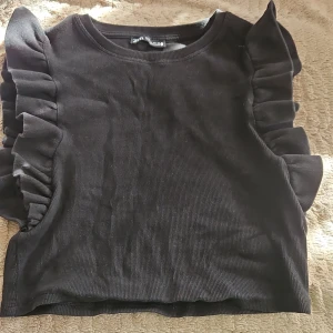 Svart topp med volangärmar - Svart ribbad topp från Zara med volangdetaljer längs ärmarna. 