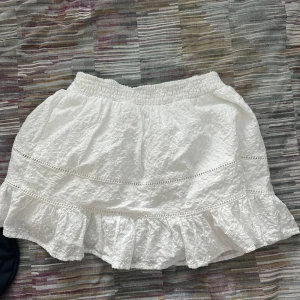 Vit volangkjol med spetsdetaljer - Supersöt vit kortkjol med volanger och spetsdetaljer. Kjolen har resår i midjan och är gjord i ett lätt, krispigt bomullstyg. Perfekt för sommarens alla äventyr och ger en romantisk vibe till din outfit. ALDRIG ANVÄND