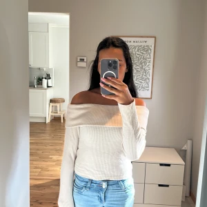 Offshoulder ribbad ljusbeige tröja - Snygg offshoulder tröja i ljusbeige med ribbad struktur. Tröjan har långa ärmar och sitter tight mot kroppen, vilket ger en clean och modern look. Perfekt att matcha med jeans eller kjol för en chill stil. Materialet är mjukt och stretchigt, vilket gör den skön att bära. 