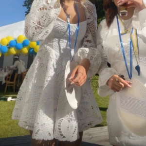 Vit spetsklänning från Boohoo - Superfin vit kortklänning från Boohoo med puffiga långärmar och v-ringad hals. Klänningen har ett detaljerat spetsmönster och sitter snyggt med en normal passform. Perfekt till student eller sommarens alla tillfällen!