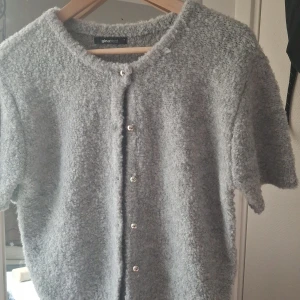 Grå kofta från Gina Tricot med knappar - Mysig grå kofta från Gina Tricot i storlek S. Koftan har korta ärmar, rund hals och är tillverkad i ett fluffigt stickat material. Stängs med silvriga knappar framtill och har en loose passform som ger en chill vibe.använd en gång💗