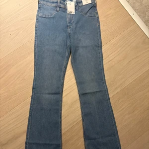 Blå flared jeans från H&M, låg midja - Snygga ljusblå jeans från H&M med flared ben och låg midja. Modellen har klassisk femficksdesign och justerbar midja för extra komfort. Perfekta för dig som gillar retrovibbar och vill ha en cool siluett. Materialet är mjukt denim i bomull.