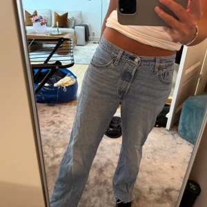 Levis 501 ljusblå jeans med rå kant - Säljer ett par klassiska Levis 501 jeans i ljusblå tvätt. Modellen har rak passform, låg midja och fem fickor. Jeansen är i denim och har en rå, fransad kant längst ner för en chill vibe. Perfekta för dig som gillar en avslappnad och tidlös look.