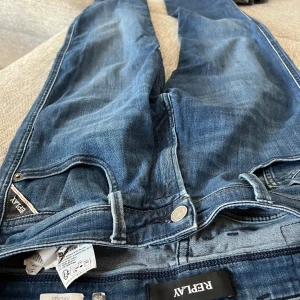 Replay Anbass blå jeans, storlek 29/32 - Säljer ett par snygga Replay Anbass jeans i klassisk blå tvätt. Modellen har raka ben, fem fickor och detaljerade sömmar på bakfickan. Jeansen är tillverkade i mjukt bomullsmaterial med en skön passform och har Replay-logga vid fickan.