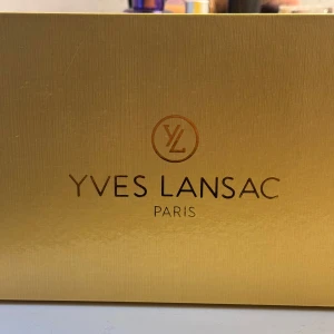 Gul kuvertväska från Yves Lansac - Snygg gul kuvertväska från Yves Lansac Paris med croco-mönstrad yta och guldfärgade metalldetaljer. Väskan har en kedja som axelrem och ett stort YL-emblem framtill. Kedjan går lika bra att ta av om man skulle vilja det!🤗 Använd ungefär 3 ggr💛(Skickar såklart med boxen)