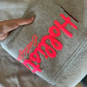 Grå mjukisbyxor från Hollister - grå mjukisbyxor från Hollister med stor rosa broderad logga längs benet. Byxorna har en avslappnad passform och är gjorda i mjukt bomullsmaterial. Står att byxorna är i storlek L men skulle nog mer säga att dom är S. Nyskick 💝💕💖