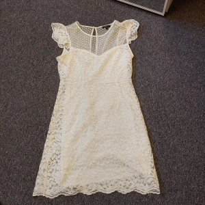 Vit spetsklänning från Xaul Edition - Supersöt vit kortklänning från Xaul Edition i storlek 38. Klänningen har spetsmaterial med blommigt mönster och transparent parti upptill med prickigt mönster. Korta volangärmar och rund halsringning ger en romantisk vibe. Perfekt för dig som gillar detaljer och feminin stil.  Finns i Karlstad 😄