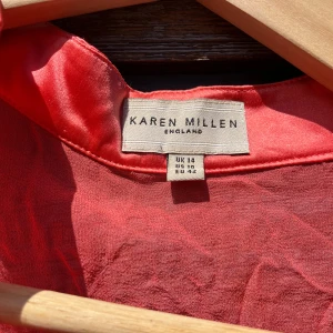 Aprikosfärgad blus med rosett från Karen Millen - Snygg aprikosfärgad blus från Karen Millen med transparenta långärmar och en stor rosett vid halsen. Blusen har v-ringad front och är gjord i glansigt sidenmaterial som ger en lyxig vibe. Perfekt för dig som vill sticka ut med en cool och feminin look. 250kr (priset kan diskuteras)