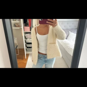 Mohair kofta - Mysig och fluffig beige kofta med två stora fickor framtill. Koftan har lång ärm och är öppen framtill utan knappar eller dragkedja. Den är stickad och har en loose passform som ger en chill vibe. Perfekt att slänga på över en t-shirt eller linne.