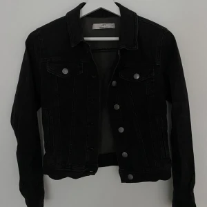 Svart jeansjacka från JDY XS - Svart jeansjacka från JDY i storlek XS. Klassisk modell med silverfärgade knappar framtill, två bröstfickor med lock och långa ärmar. Snygg krage och raka linjer ger en clean look. Perfekt att slänga över en hoodie eller t-shirt för en chill vibe.
