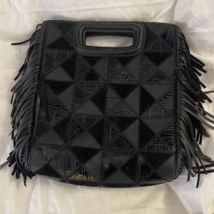 Maje handväska -  svart handväska från Maje i skinn med fransar längs sidorna och ett snyggt mönster på ena sidan, köpt för ungefär 4000 kronor i majes egna butik på drottninggatan, säljer då den inte kommer till användning längre! Inga defekter förutom självaste Maje märket vid handttaget som blivit lite utsuddat men inget som märks av! Hör av er vid funderingar å frågor🥰