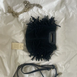 Blå fransad axelväska från Maje - Cool blå axelväska från Maje i mocka med fransar längs kanterna och ett robust handtag. Väskan har både en lång axelrem i skinn och en chunky silverkedja som kan användas som axelrem. Perfekt för dig som gillar statement-accessoarer. Visa fläckar men går och få bort med mocka borste.