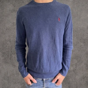 Blå långärmad tröja Polo Ralph Lauren - Klassisk marinblå långärmad tröja från Polo Ralph Lauren i mjuk pima bomull. Tröjan har rund halsringning och den ikoniska röda broderade loggan på bröstet. Perfekt för en clean och stilren look.
