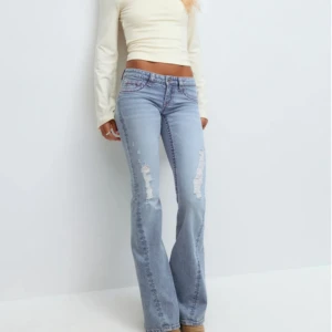 GINA Bootcut ljusblå jeans med slitningar - Snygga ljusblå bootcut jeans med slitna detaljer på benen. Jeansen har klassisk femficksdesign och låg midja, vilket ger en avslappnad och trendig vibe. HELT NYA MED PRISLAPP! storlek S