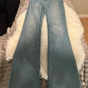Bootcut ljusblå jeans - Säljer ett par ljusblå bootcut jeans med snyggt broderi i rosa från Nelly!