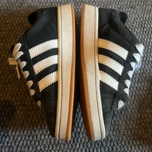 Adidas Campus svart/vit sneakers 36 - Säljer ett par Adidas Campus sneakers i svart mocka med klassiska vita ränder och vit sula med gummidetalj. Skorna har rund tå, platt sula och vita snören. Inga svarta skosnören med.