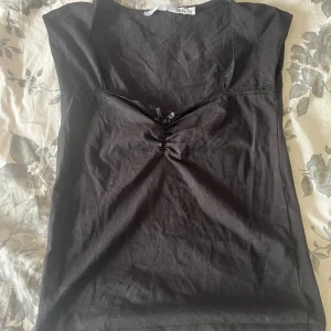 Svart ärmlös topp med spets och rosett - Svart ärmlös topp från Lager 157 som har spets och en liten söt rosett på framsidan. Toppen har rynkdetalj vid bysten och är gjord i  bomull.