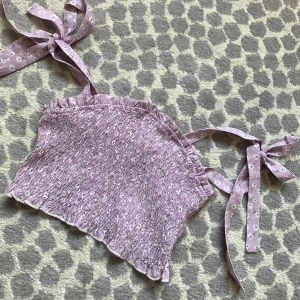 Ljuslila blommig bandeau topp med knyt - Supersöt bandeau topp i ljuslila med små vita blommor och smockad struktur. Axelbandslös modell med breda band som knyts på axlarna för extra gullig vibe. Perfekt för varma dagar och ger en riktigt somrig känsla. Passar mer som xs-s.