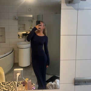 Marinblå långklänning med öppen rygg - Säljer en marinblå långklänning från Gina med tight passform och långa ärmar. Klänningen har en snygg öppen rygg som ger en cool och elegant vibe. Materialet är mjukt och stretchigt, vilket gör den superbekväm att bära. Oanvänd med prislapp kvar