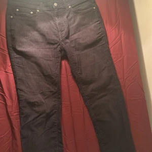 Svarta manchesterbyxor från Dressmann - Säljer ett par svarta manchesterbyxor från Dressmann med klassisk femficksdesign och raka ben. Byxorna har tydlig ribbad struktur och silverfärgade nitar vid fickorna. Perfekt för dig som gillar en stilren och tidlös look.