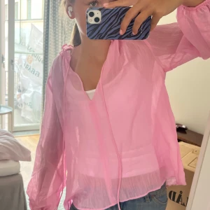 Rosa blus från Zara - Säljer en superfin ljusrosa blus från Zara med v-ringad hals och tunna knytband vid kragen. Kan även användas som beach coverup!