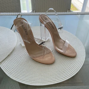 Klara sandaler med transparent klack Boohoo - Säljer ett par sandaler från Boohoo i storlek 36 med nude-färgad sula och transparenta remmar. Klacken är hög och helt genomskinlig, vilket ger en modern och edgy vibe. Perfekt för dig som gillar statement-skor med unik design och vill sticka ut.
