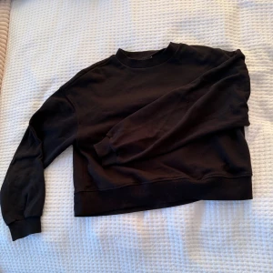 Svart sweatshirt - En svart sweatshirt med rund hals och långa ärmar. Tröjan har ribbade muddar vid ärmslut och nederkant, vilket ger en skön och avslappnad vibe. Perfekt att matcha med jeans eller mjukisbyxor för en chill look.