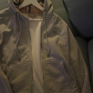 Grå Burberry hoodie med rutig huva - ‼️JAG TAR BYTEN‼️Säljer en grå hoodie från Burberry i helt perfekt skick inte ens en liten fläck med klassisk rutig insida i huvan och dragkedja framtill. Tröjan har snörning vid huvan, två fickor och ett diskret Burberry-logomärke på bröstet. Perfekt för dig som gillar stilrena och lyxiga streetwear-plagg.. Den är i helt perfekt skick exakt som ny skriv till mig om ni har något ni vill byta💯Jag möts upp också. Kan mötas upp samma dag som mi skriver.