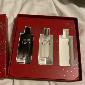 Byter! - Snyggt parfymset från Giorgio Armani med två flaskor Acqua di Giò. En svart flaska och en frostad vit flaska, båda i stilren design. Kommer i en röd presentask med silverprickar – perfekt för dig som gillar exklusiva dofter.