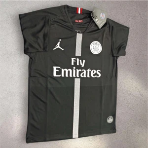 Svart PSG fotbollströja Jordan x Fly Emirates - Svart PSG fotbollströja med vit vertikal rand och tryckta loggor från Jordan och Paris Saint-Germain. Fly Emirates sponsortryck på bröstet. Kortärmad modell i lätt och ventilerande material, perfekt för match eller träning.