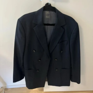 Mörkblå kavaj Tiger of Sweden 48 - Dubbelknäppt mörkblå kavaj från Tiger of Sweden i klassisk modell med breda slag och flera fickor. Kavajen är fodrad med slätt tyg och har snygga knappar framtill. Perfekt för dig som gillar stilrena och tidlösa plagg.