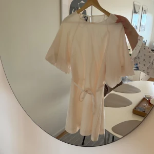 Miniklänning från &other stories - Säljer en helt ny klänning från & Other Stories i en ljusrosa/beige nyans. I stl L. Med knyt i midjan.  Den är endast provad, aldrig använd. När jag köpte den fanns en liten sminkfläck vid kragen (se bild), men den går med största sannolikhet bort med galltvål. Jag har inte tvättat den själv än, men kan självklart göra det och uppdatera hur fläcken ser ut innan köp.  Nypris: ca 880 kr 