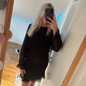 Svart kort klänning med volang - Säljer en jättefin klänning från Kappahl som passar perfekt till finare tillfällen. Klänningen har genomskinliga ärmar och en tajtare del vid magen och nedåt. Finns även fina volanger vid klänningens slut. Det är storlek 158 men passar xs bra. 