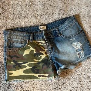 Camouflage jeansshorts från Gina tricot - jeansshorts med en unik design. Den ena sidan är i klassisk denim med slitningar, medan den andra sidan har ett camouflagemönster. Strl 38