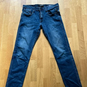 Replay Anbass blå jeans, storlek 31 - Snygga blå jeans från Replay, modell Anbass. Klassisk femficksdesign med raka ben och normal passform. Jeansen har en mörkblå tvätt med lätt slitning och är tillverkade i mjukt bomullsmaterial med stretch för extra komfort. Perfekta för en avslappnad och cool stil.
