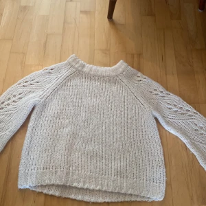 Vit stickad tröja med hålmönster - Säljer en vit stickad tröja från Cubus i storlek 146/152. Tröjan har långärmade ärmar med snyggt hålmönster och grov ribbstickning vid hals, ärmslut och nederkant. Perfekt för dig som gillar mysiga och stilrena plagg med lite extra detaljer.