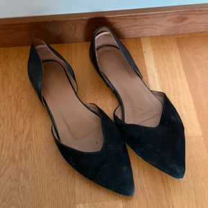 FLATTERED ballerinaskor med spetsig tå - 100% läder / mocka. Snygga svarta ballerinaskor från Flattered med spetsig tå och platt sula. Skorna har en stilren design med öppen sida och är tillverkade i mocka och skinn. Perfekta för dig som gillar minimalistisk och trendig look.