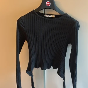Svart ribbad croppad topp NA-KD - Svart långärmad topp från NA-KD i ribbad bomull med croppad passform och snygg knytning baktill. Perfekt för dig som gillar stilrena och trendiga plagg. Aldrig använd💕