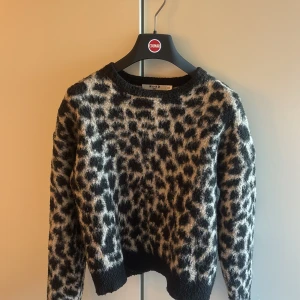 Leopardmönstrad stickad tröja NA-KD - Säljer en fluffig stickad tröja från NA-KD i storlek XXS med leopardmönster i svart och beige. Tröjan har rund hals, långa ärmar och ribbade muddar vid hals, ärmslut och nederkant. Perfekt för dig som gillar djurmönster och vill ha en mysig tröja. Den är väl använd därav priset💕storlek xxs men passar både xs o s