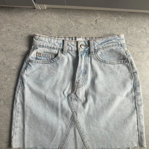 Ljusblå jeanskjol från Denim Co. - Säljer en oanvänd ljusblå jeanskjol från Denim Co. med klassisk femficksdesign, knapp och dragkedja framtill samt rå kant nedtill. Kjolen har en rak passform och är kort i modellen, perfekt för dig som gillar en chill och enkel stil. Skickar iväg samma dag eller dagen efter🙌🏼