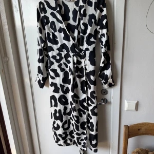 Svartvit omlottklänning från ASOS - Säljer en lång omlottklänning från ASOS med svartvitt leopardmönster. Klänningen har långa ärmar, knyt i midjan och är tillverkad i mjuk polyester. Perfekt för dig som gillar statement-plagg med coola mönster och snygg passform.