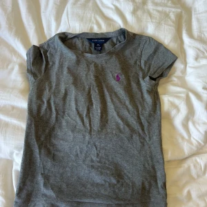 Grå t-shirt från Ralph Lauren - Grå t-shirt från Ralph Lauren med klassisk rund hals och korta ärmar. Storlek 8-10 år men har själv andvänt den som 14åring som en thight t shirt. Superfin till skolstarten. Köpte på plock för ca ett halvår sen för 200kr säljer för 100kr!